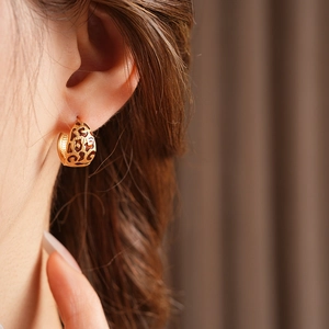 Macro shot of gold leopard print cutout hoop earrings worn by a female model