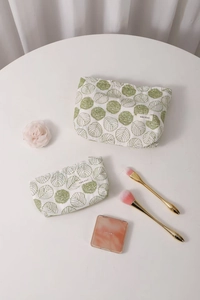 Close-up of white linen cosmetic bags with green leaf embroidery and zipper detail