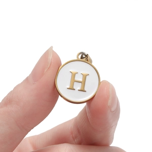 Detail view of round gold stainless steel pendant with white enamel letter H charm