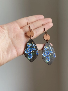 Detail of wooden drop earrings with blue daisy print and retro metallic ear hooks