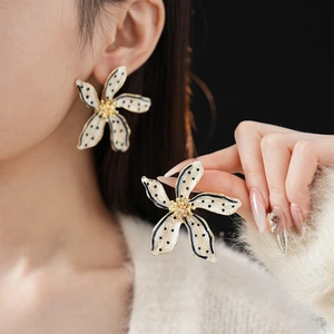 Detail of vintage beige floral earrings with black polka dots and gold trim on model