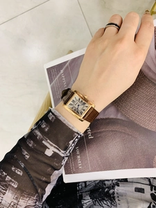 Elegant woman wearing rectangular gold watch with brown leather strap and roman numerals