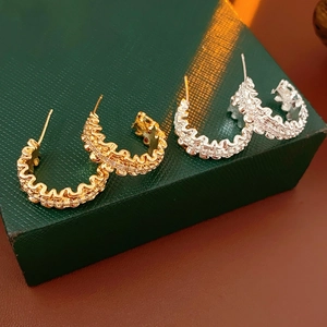 Macro detail of wave textured C-shape earrings with zircon inlay in gold and silver finish