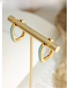 Macro shot of geometric gold earrings with light blue enamel on a jewelry display stand