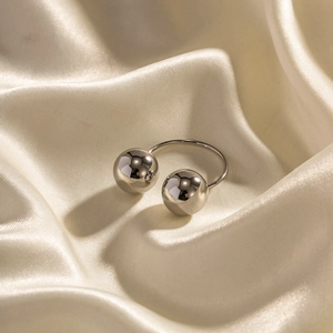 Polished silver stainless steel open ring with two large spheres on beige silk background