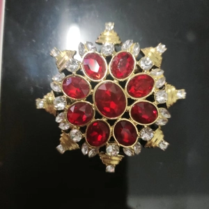 Macro detail of red gemstone flower brooch with crystals on a black reflective surface