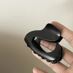 Detail showing a large matte black shark hair claw clip with a sleek curved design