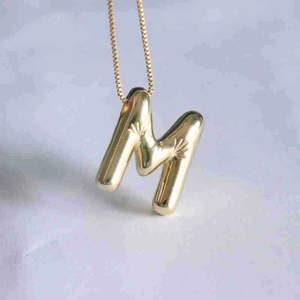 Macro shot of 3D balloon style letter M pendant with starburst texture on gold chain