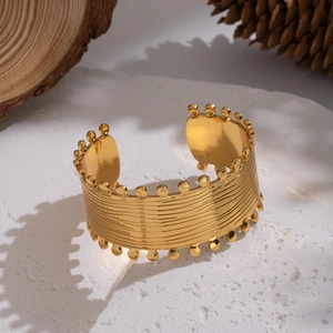 Detail of 18K gold plated wide water wave bangle with beaded edges on a stone base
