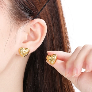 Close-up of golden heart earrings with diamond accents and textured pattern on model
