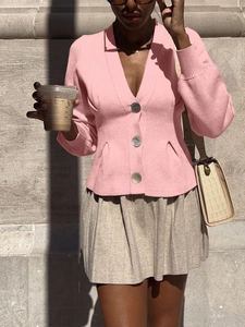 Detail of pink knitted V-neck cardigan with three buttons paired with a beige pleated skirt