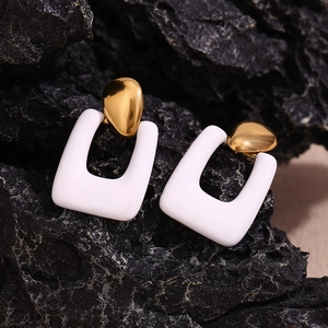Detailed shot of gold-plated geometric earrings with white enamel on a black stone surface