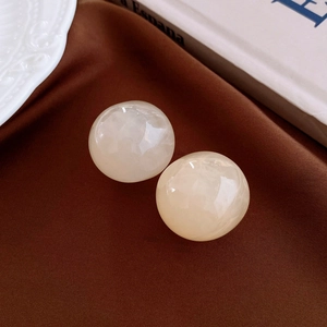 Detail view of round cream resin earrings with marble texture on elegant silk background