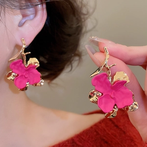 Detail of flower earrings with gold branches and rose red petals on a female model