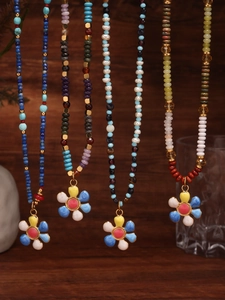 Detail showing colorful beaded necklaces with enamel flower pendants on wooden background