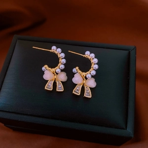 Close-up of golden C-shaped pearl earrings with pink bow and rectangular zircon details