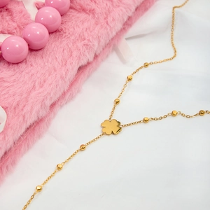 Détail d'un pendentif trèfle doré sur chaîne à billes avec décor en velours rose