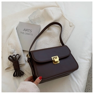 Dettaglio di una borsa a tracolla in pelle marrone scuro con fibbia quadrata dorata su bianco