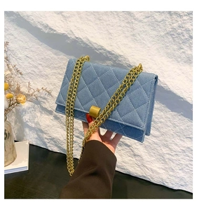 Detail of blue denim quilted square bag with elegant gold metal chain shoulder strap