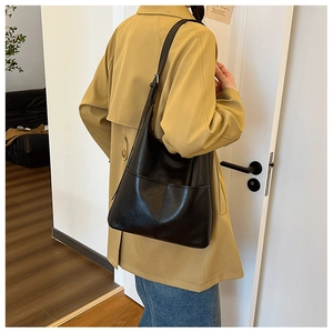 Grand sac cabas en cuir noir avec large bandoulière porté par un mannequin en studio