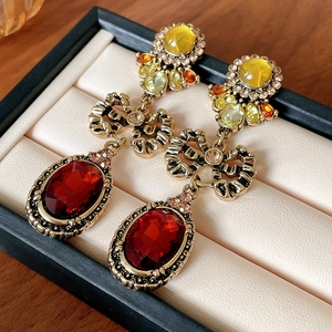 Dettaglio di orecchini vintage a fiocco dorato con gemma rossa e design barocco