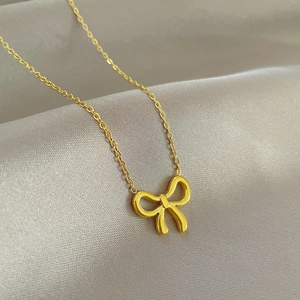Macro shot of a golden bow pendant on a delicate titanium steel chain over silk fabric