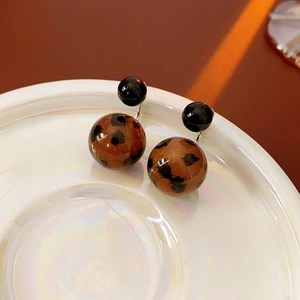 Close-up of leopard print and black resin ball drop earrings on a pearl luster tray