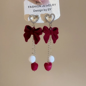 Close-up of vintage heart stud earrings with burgundy velvet tassels and plush white pom-poms