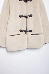 Dettaglio cappotto in pelliccia sintetica con alamari e finiture in pelle scura