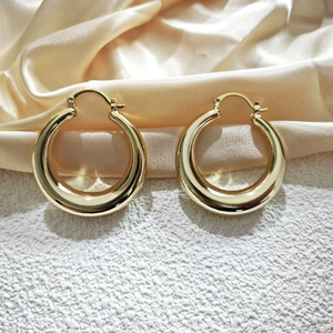Detailed macro view of 18K gold-plated hollow hoop earrings on luxury silk fabric background