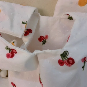 Detail of white textured fabric bag with embroidered cherry patterns and dot weave