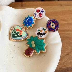 Detail of colorful enamel heart and sun earrings on a beige ceramic plate surface