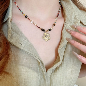 Close-up of bohemian beaded necklace with textured gold flower charm on a model
