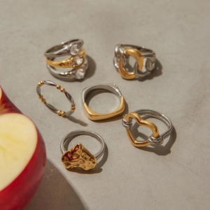 Artistic layout of various gold and silver zircon rings on textured gray background