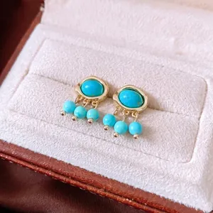 Vintage gold turquoise earrings with oval pendants and beaded details on white velvet