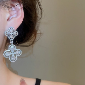 Close-up of a silver clover drop earring with zircon crystals on a female model