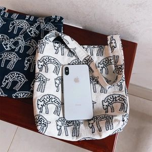 Canvas handbag size comparison with iPhone on wood bench featuring sheep patterns