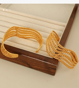 Macro detail of multi-layer golden wave bangles with textured finish on a wooden tray
