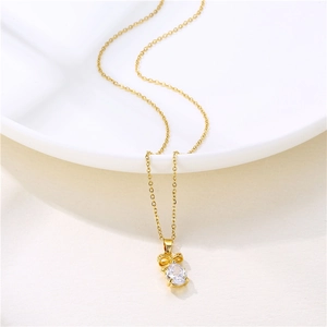 Golden necklace with a bow pendant and teardrop zircon gemstone on white ceramic plate