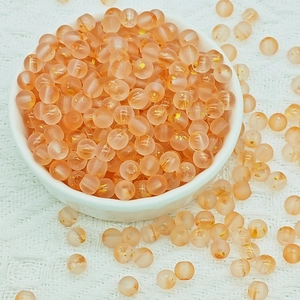 Detailed macro view of frosted orange-pink glass beads with gold foil in a ceramic bowl