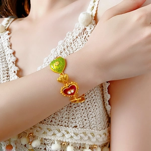 Detail of vintage gold bracelet with green and red enamel hearts and pearls on wrist