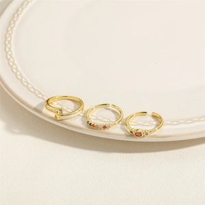 Three gold rings with colorful zircons and gemstones on a textured white plate