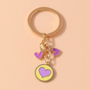 Detail of a golden keychain featuring three heart pendants with purple enamel finish