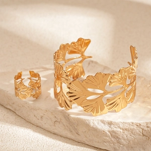 Détail du bracelet manchette ginkgo doré et de la bague assortie sur un socle en pierre