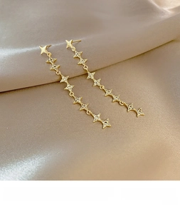 Detailed close-up of golden star drop earrings with zircons on elegant silk background