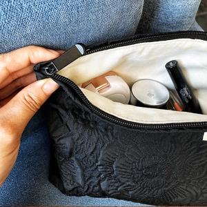 Detail of hand opening black jacquard makeup bag showing spacious interior with cosmetics