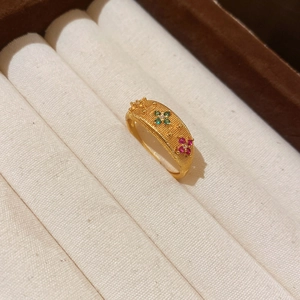 Macro shot of gold floral ring featuring woven texture with green and pink zircons