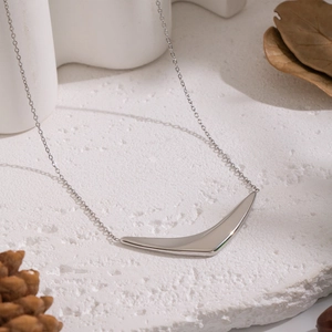 Close-up of a silver curved pendant necklace on a textured white surface with soft light
