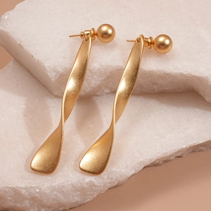Detailed view of golden twisted metal earrings with round studs on a textured stone