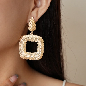 Detail of gold geometric square earrings with wheat leaf texture on a model side profile